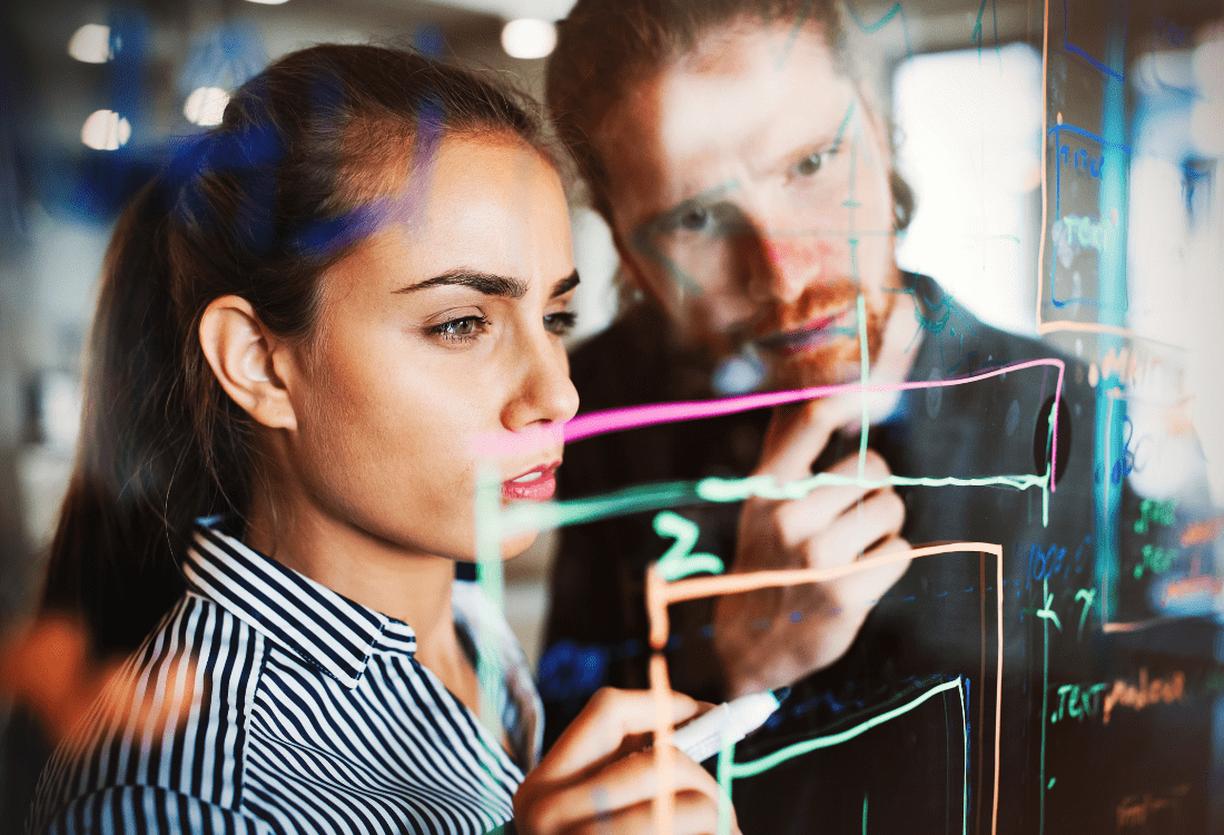 Two app developers writing ideas on a board to show the potential pitfalls and app development issues they need to avoid.